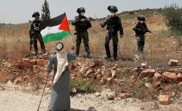 فلسطيني يرفع علم فلسطين في وجه الاحتلال